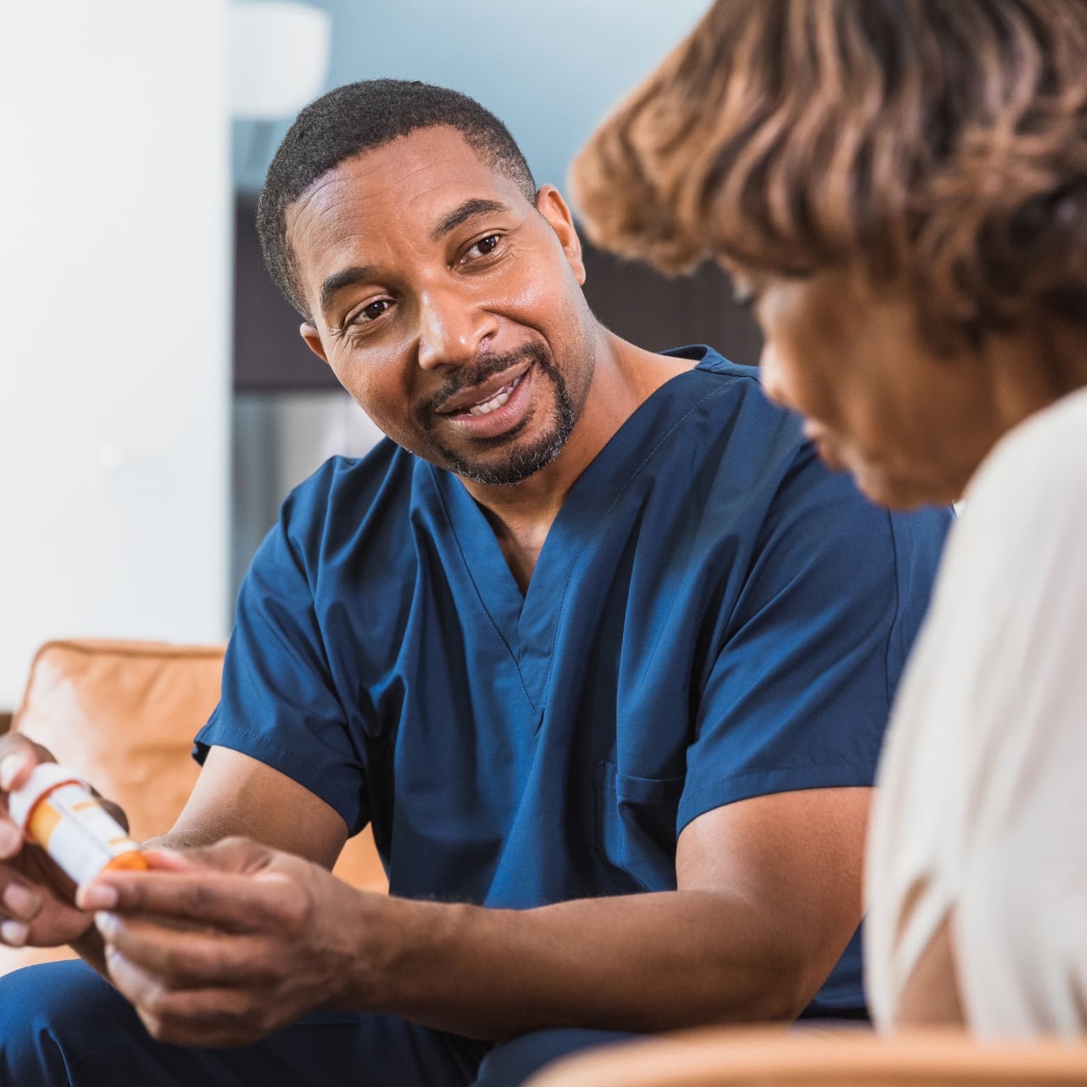 A male nurse in navy scrubs reviewing medication with an older woman at home